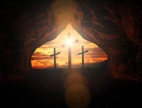 3 Kreuze steht am Ende einer Höhle. Von hinten scheint Sonne die Kreuze an.